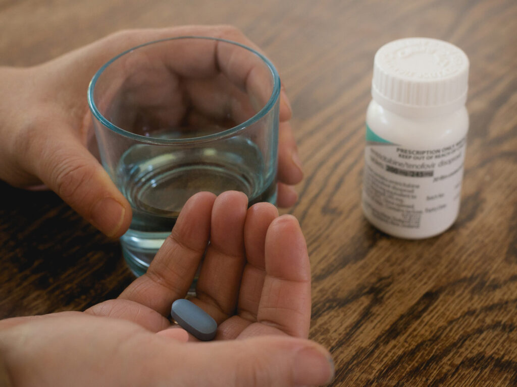 Close-up photo of someone holding a pill in their hand, with a bottle of pills in the background