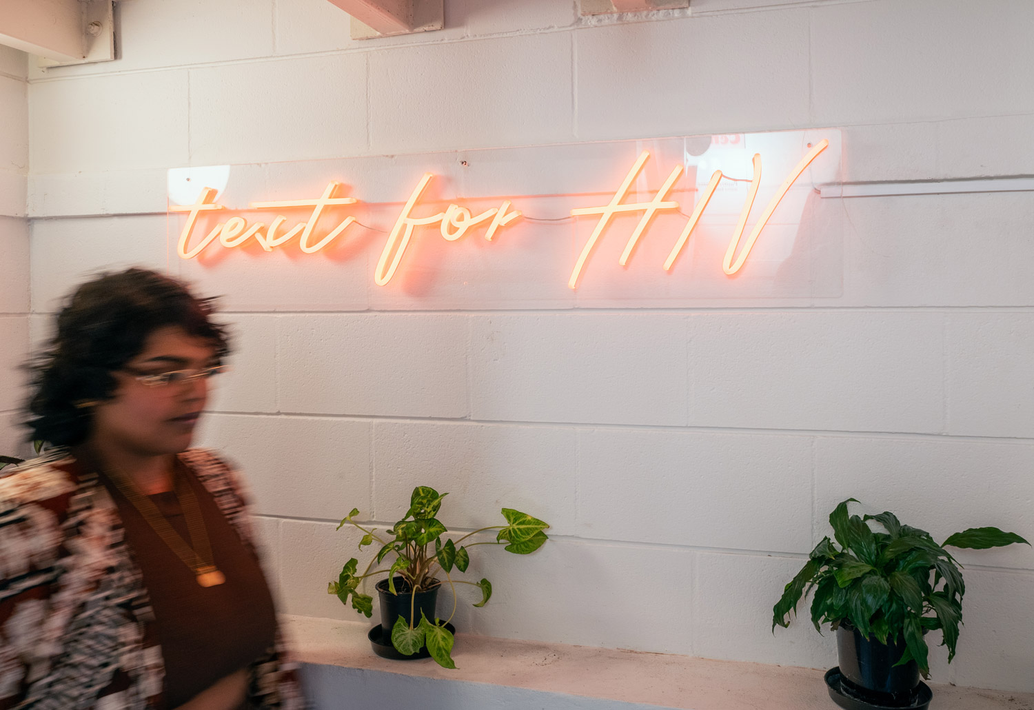 Photo of someone walking past a neon sign with the words "test for HIV"