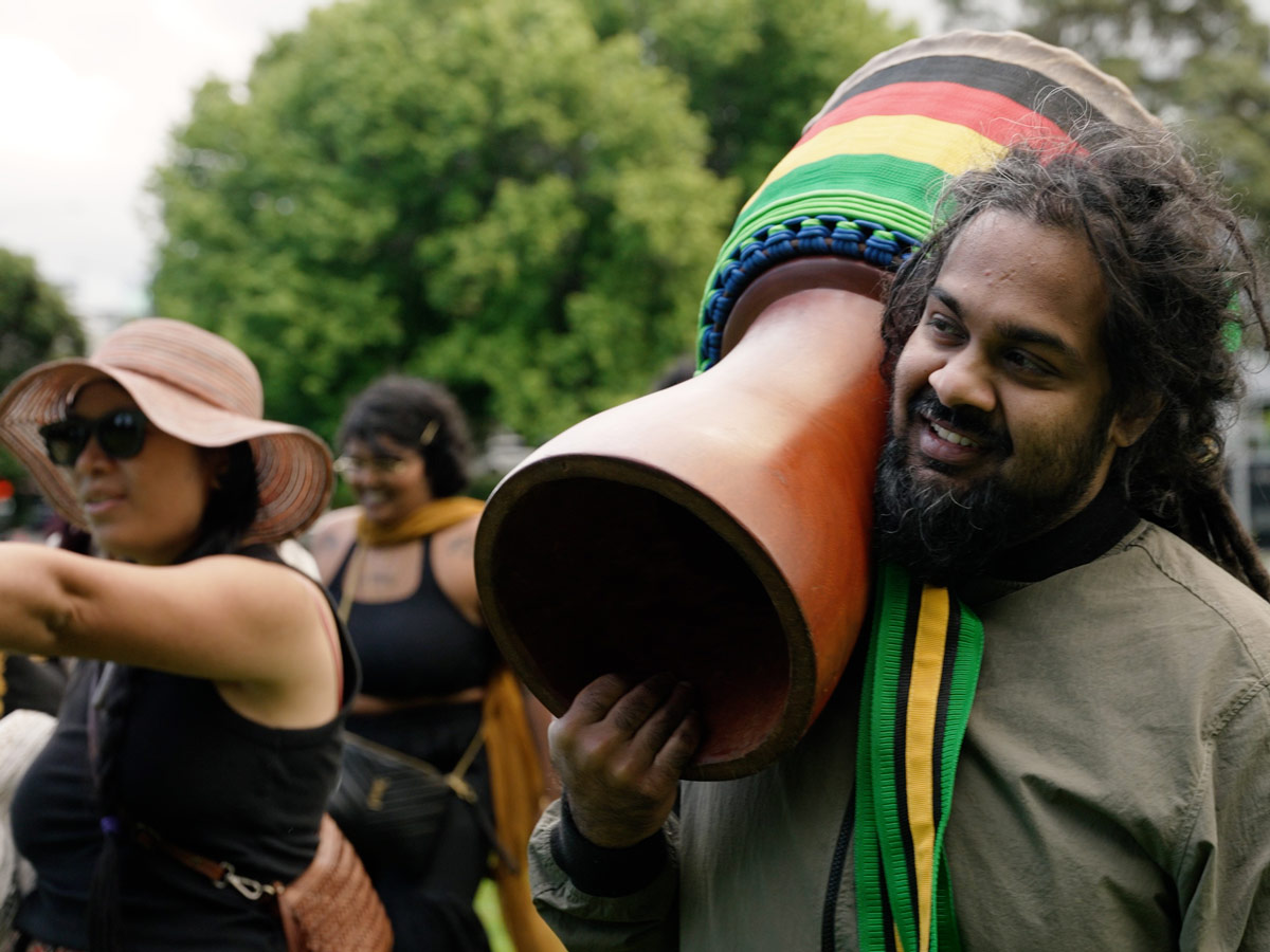 Photo of a person walking through an Auckland park, holding an African drum